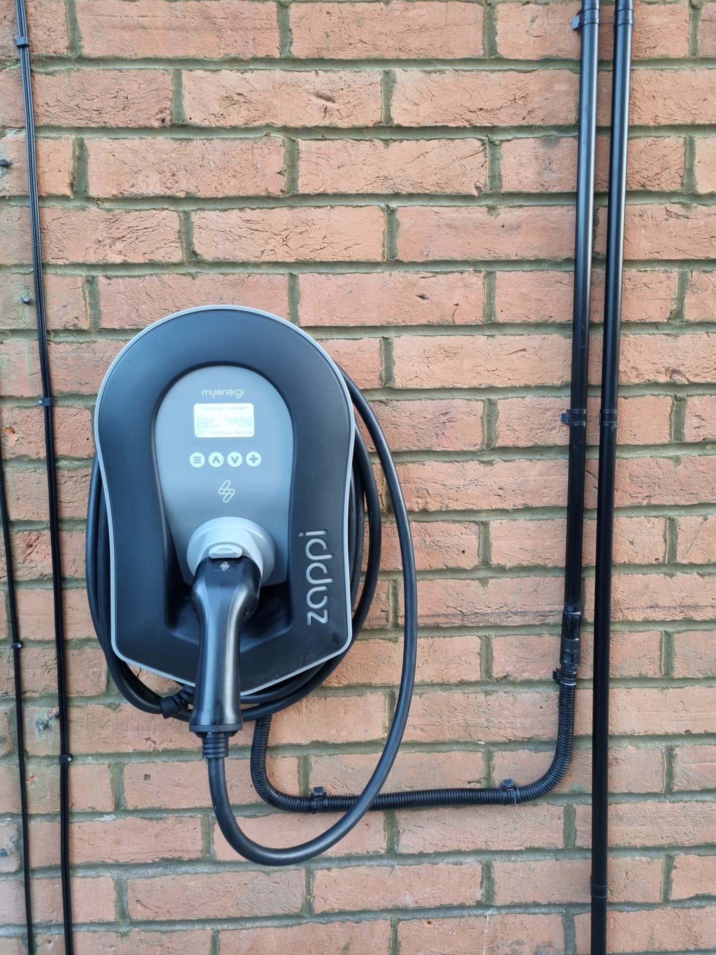 Zappi EV charger installed on a red brick wall with neat cable containment