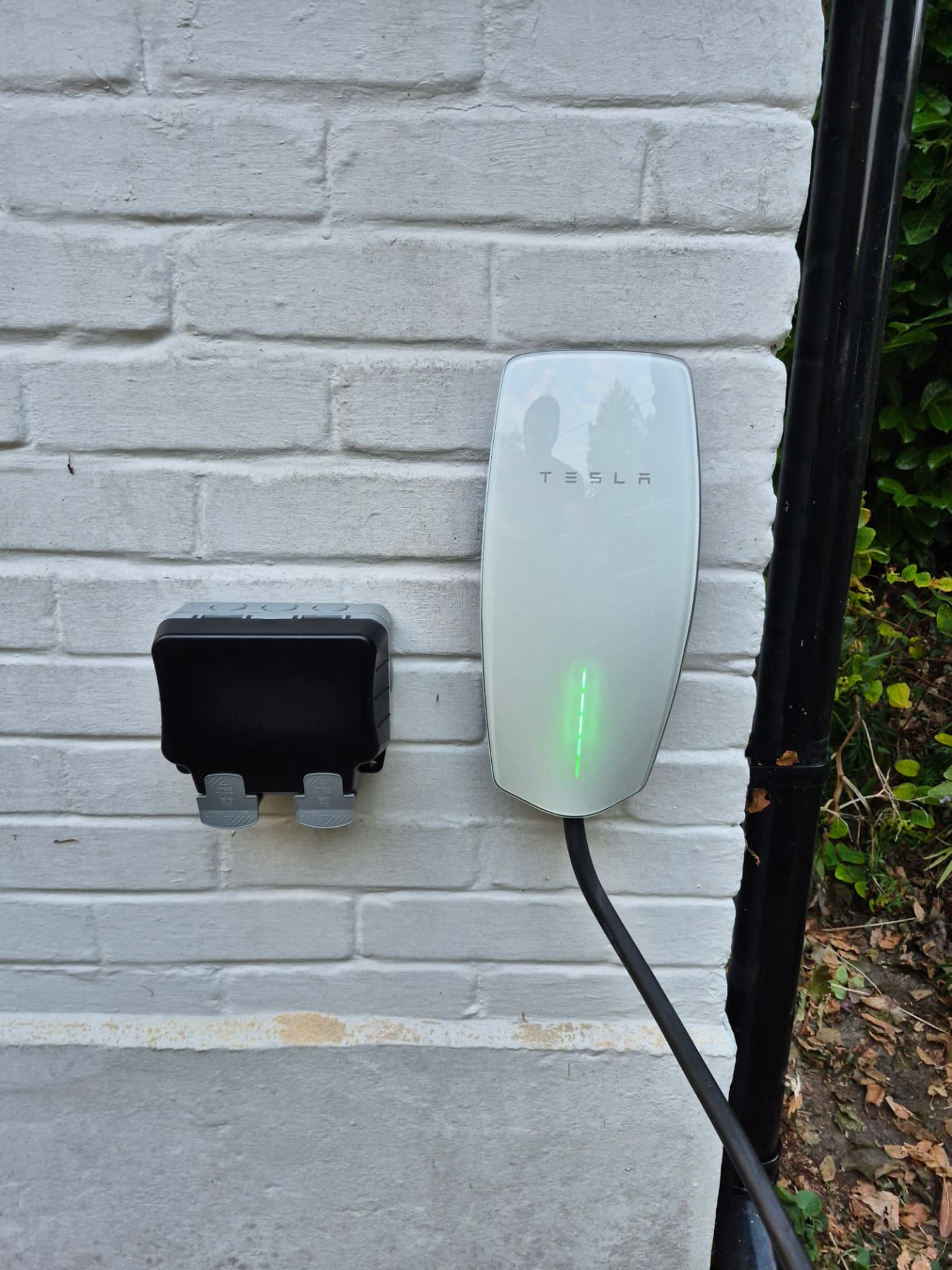 Tesla wall connector and outdoor socket on a white painted wall