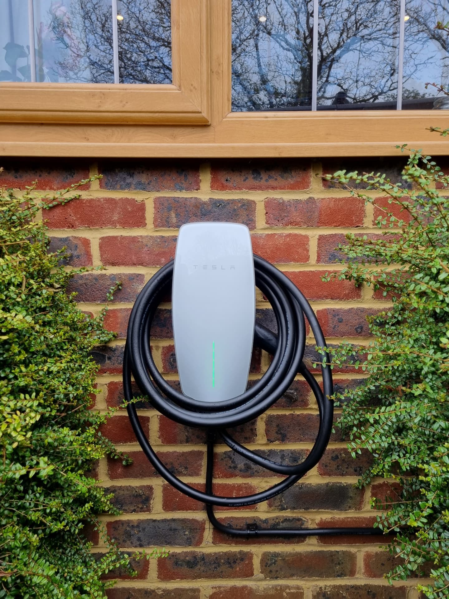 Electric car charging from a wall-mounted EV charger on a driveway